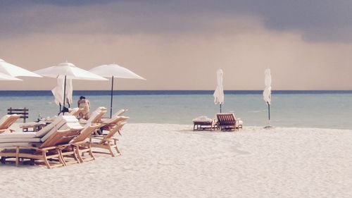 Deck chairs on beach against sky