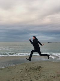 Full length of man sitting on beach against sky