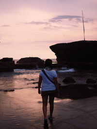 Rear view of man standing on rock at beach against sky