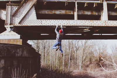 Rear view of young man with long hair climbing abandoned railway bridge