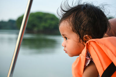 Close-up of baby boy wearing life jacket against lake