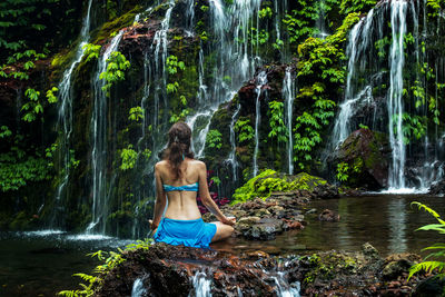 Rear view of woman meditating against waterfall