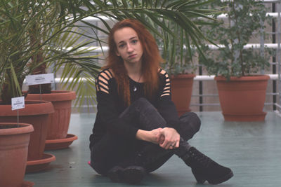 Full length portrait of sad young woman sitting by potted plants