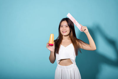 Portrait of smiling young woman drinking glass against blue background