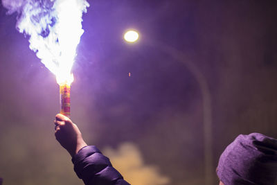 Low angle view of hand holding illuminated lighting equipment against sky