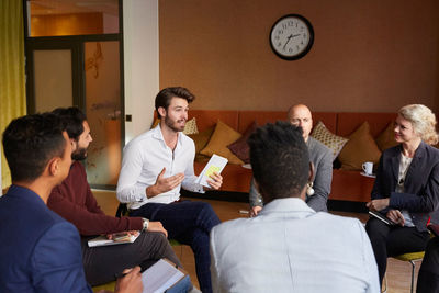 Male entrepreneurs discussing with coworkers while sitting in circle during office workshop