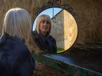 Reflection of woman in mirror by hay bales