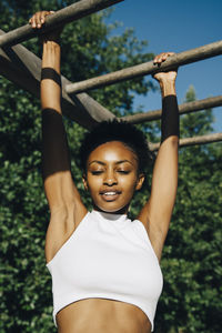 Female athlete looking down while hanging on monkey bar in park