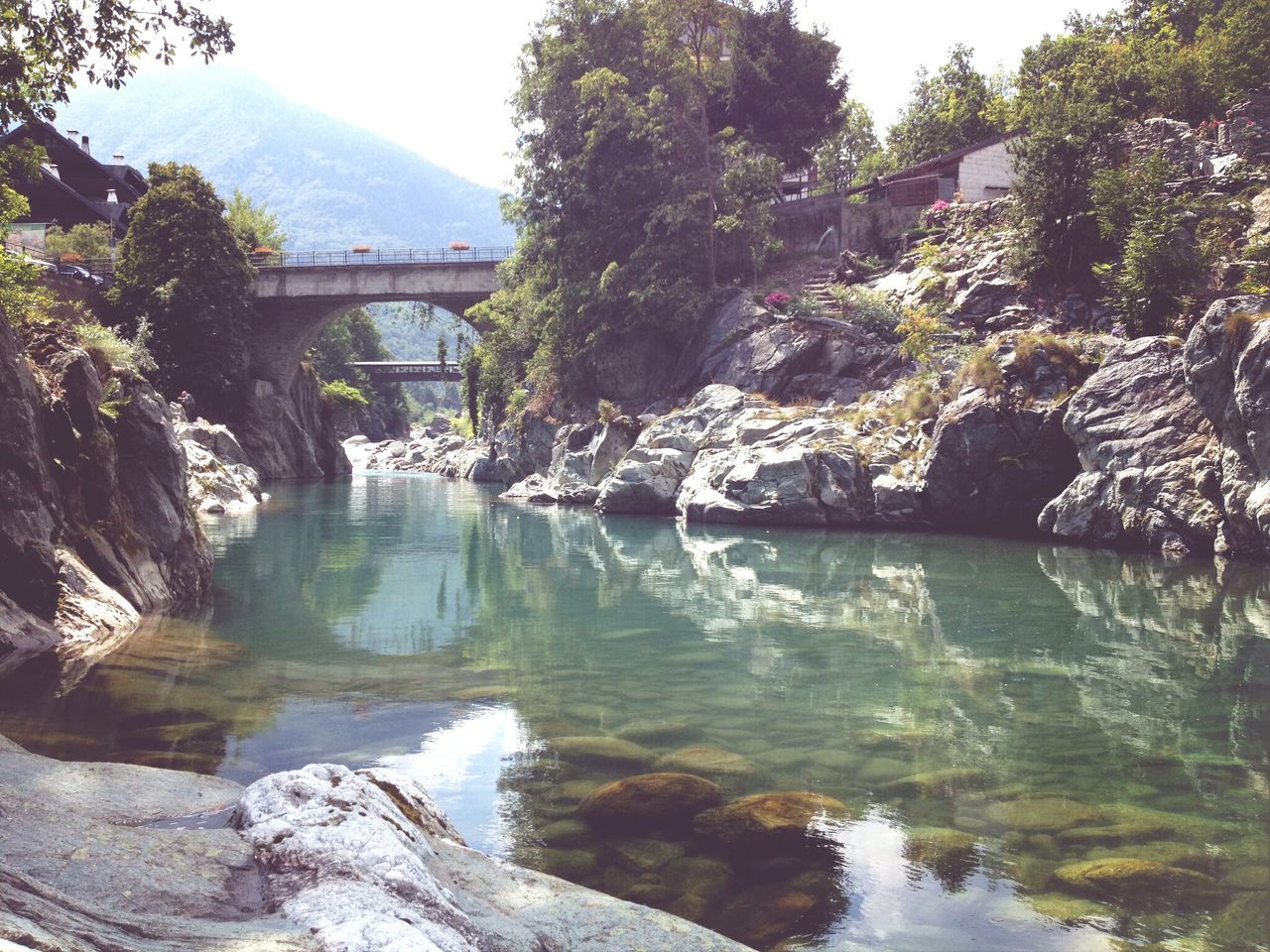 water, mountain, built structure, tree, river, architecture, bridge - man made structure, connection, rock - object, scenics, tranquility, beauty in nature, nature, waterfront, tranquil scene, reflection, clear sky, lake, flowing water, day