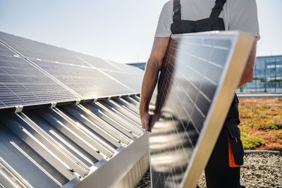 Craftsman holding a solar panel on a company building's roof, viewed from a close-up angle