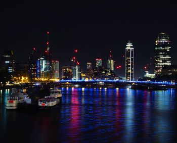 Illuminated buildings by river against sky at night