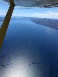 Close-up of airplane wing over sea against blue sky