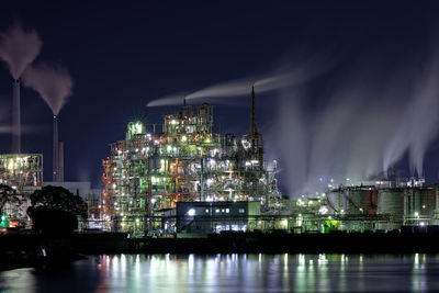 Illuminated buildings by river against sky at night