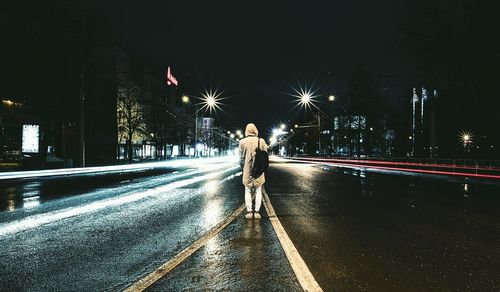 Rear view of person standing on wet road at night