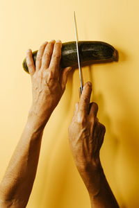 Cropped hands of woman cutting cucumber over beige background