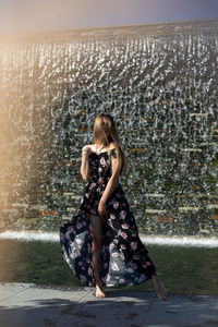 Full length portrait of woman standing against waterfall at park