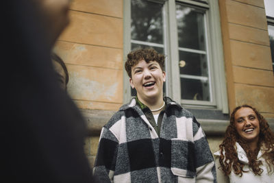 Happy boy wearing flannel shirt laughing with friends against wall