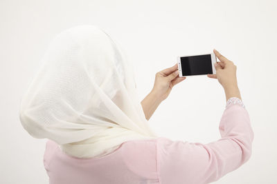 Rear view of woman taking selfie with mobile phone against white background