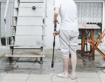 A caucasian guy in a gray sports and t-shirt from the back washes the tiles in the backyard