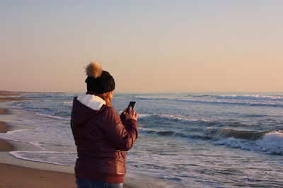 Rear view of woman photographing at beach during sunset