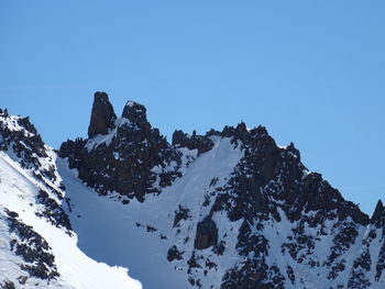 Low angle view of snowcapped mountains against clear blue sky