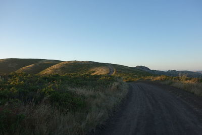 Road amidst field against clear sky