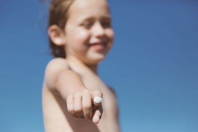 Low angle view of boy holding seashell against blue sky