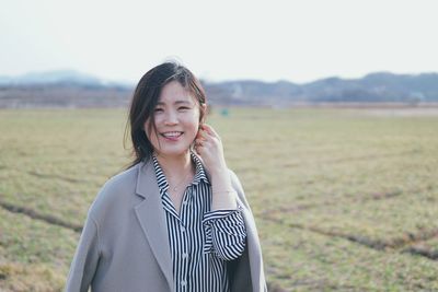 Portrait of smiling young woman standing on grassy field during winter