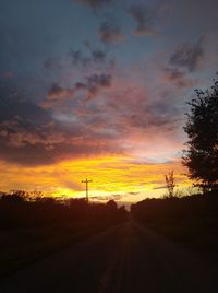 Road by silhouette trees against sky during sunset