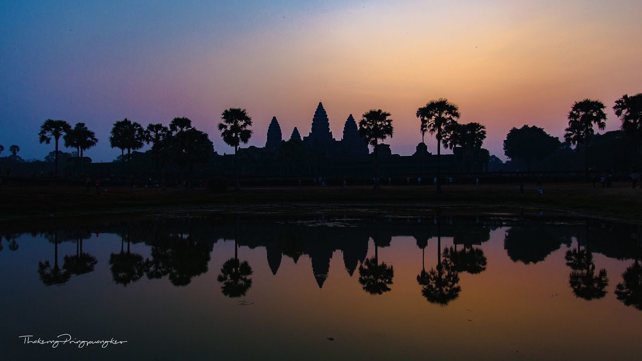 REFLECTION OF SILHOUETTE TREES IN LAKE AGAINST ORANGE SKY