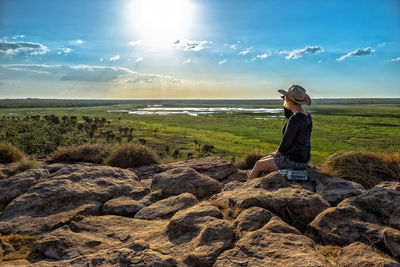 Woman sitting on rock by sea against sky