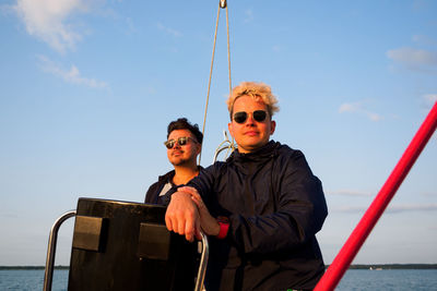 Two friends on a sailboat, one person steering wheel sailing yacht other is standing near