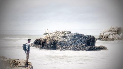 Man standing on rock by sea against sky