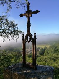 View of cross on stone structure overlooking trees and mountains against sky