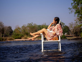 Young woman sitting on shore against clear sky