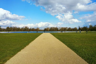 Diminishing perspective of footpath leading towards lake against cloudy sky