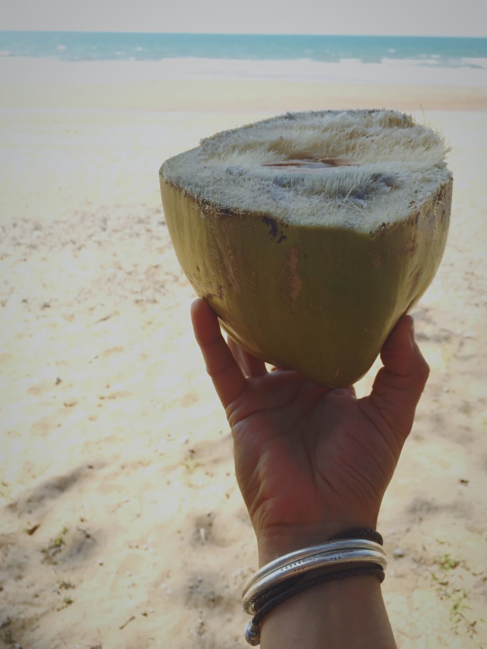 drink, food and drink, beach, refreshment, close-up, focus on foreground, holding, sand, shore, sea, freshness, lifestyles, water, outdoors, part of, sky, person