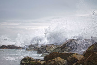 Waves splashing on rocks in sea against sky