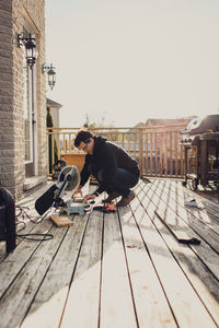 Man using a saw to fix deck boards outside of a home.