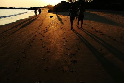 Silhouette people on beach against sky during sunset