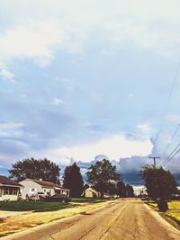 Road by trees and buildings against sky