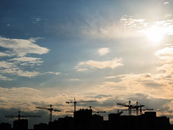 Silhouette cranes against sky during sunset