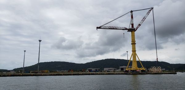 Cranes at harbor against sky