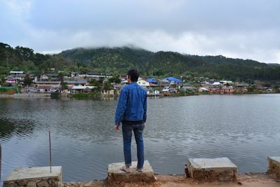 Rear view of boy standing by lake against sky