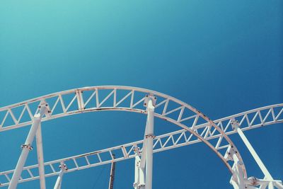 Low angle view of white rollercoaster against clear blue sky