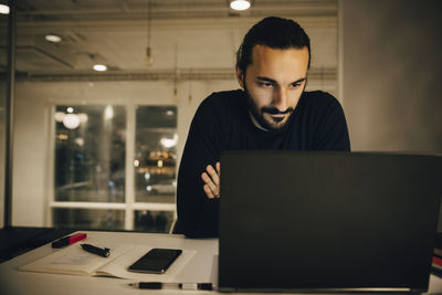 Confident businessman looking at laptop while working late in office