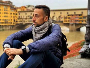 Young man looking away while sitting against bridge