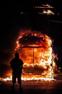 Rear view of man standing by fire at night