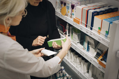 High angle view of senior customer and female owner holding medicines by rack at pharmacy store