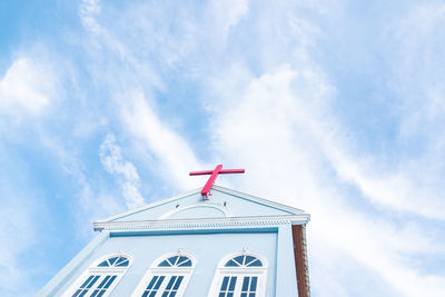 Church roof with red cross and blue sky.